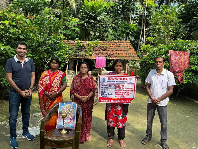 Four people holding a donation plaque for Ekal Vidyalaya in a rural Indian village setting.
